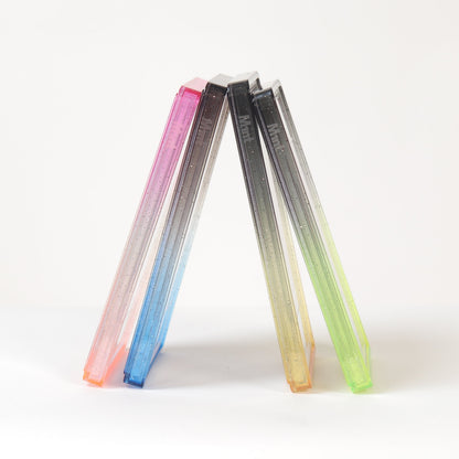 Three slim rectangular translucent items standing upright in a V shape on a white surface against a white background. The left item fades from pink to blue, the middle from black to gray, and the right from yellow to green.